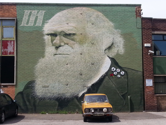Large two-storey wall mural of Charles Darwin wearing some pin badges on his lapel and a small remembrance poppy