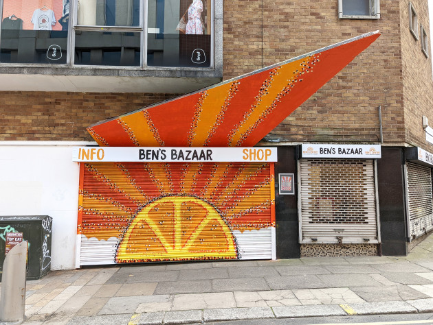 Painted shop shutters and canopy featuring a sun in the shape of an orange emerging from the clouds with sun rays projecting outwards