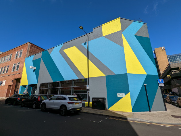Facade of the Lane7 building featuring large geometric shapes in grey, turquoise, teal and yellow