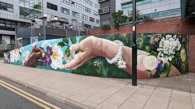 Wide mural featuring a black hand passing a purple flower to a white hand passing a white rose