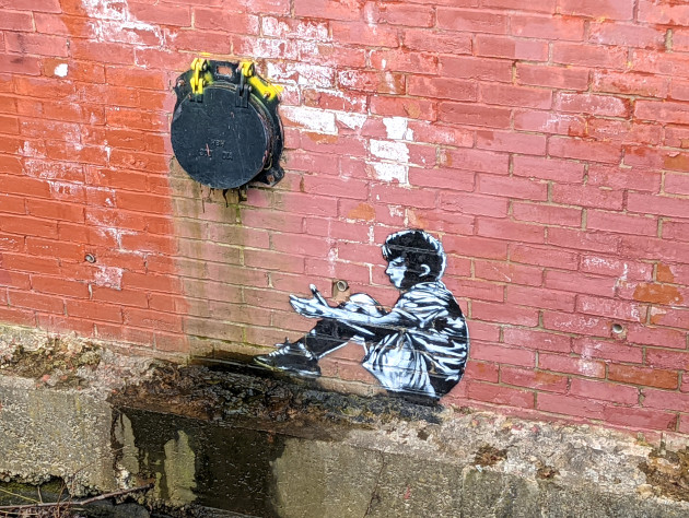 Small mural of a boy sat on the side of the riverbank wall