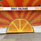 Close-up of painted shop shutters featuring a sun in the shape of an orange emerging from the clouds