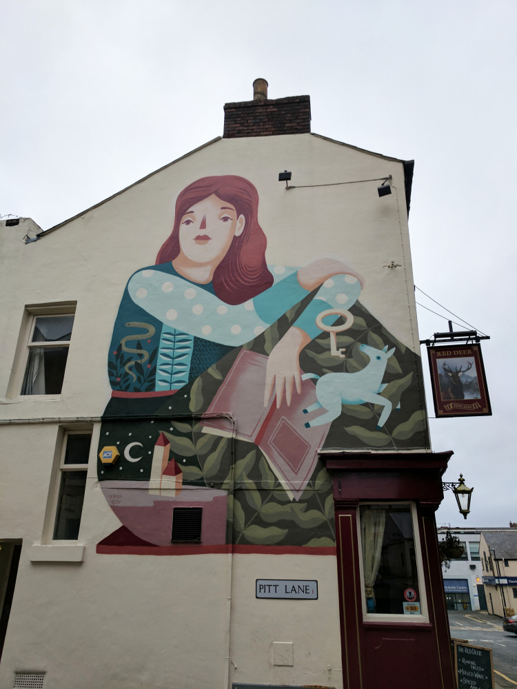 Mural of a red haired woman sat wearing a long dress looking pensive