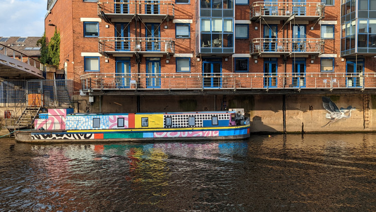 Brightly coloured river barge painted with an abstract pattern and to its side a wall mural of a grey heron