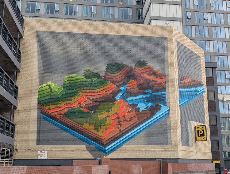 Large mural featuring a hilly landscape made up of layers split across two walls at a slight angle utilising a Trompe L’oeil effect to make it look like a flat surface