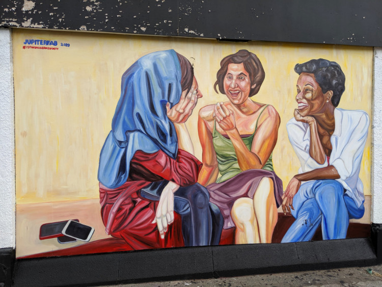 Mural depicting three women in conversation with their mobile phones stacked up behind them