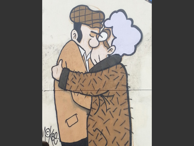 Large mural of an elderly couple embracing in a kiss; the man is wearing a jacket and flatcap, the woman is wearing a wollen coat and spectacles