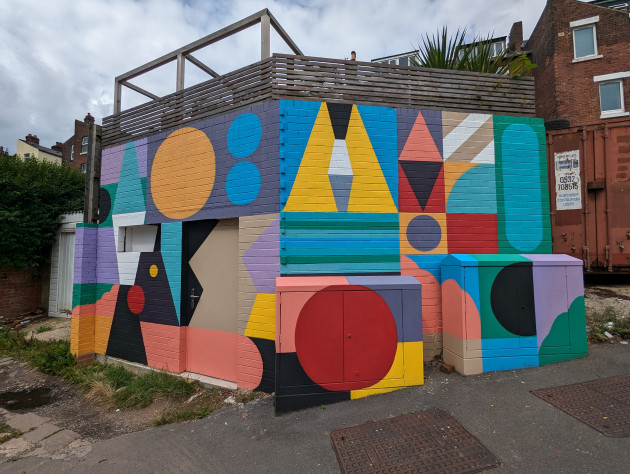 Large mural made up of colourful geometric shapes covering a large exterior building and two utility cabinets