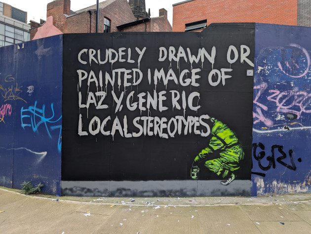 Mural of a graffiti artist crudely painting the words 'crudely drawn or painted image of lazy generic local stereotypes'