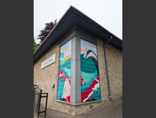 Two shutters on the corner of the library building painted with a wildlife theme featuring a badger and an owl with a trail formed of red-covered books