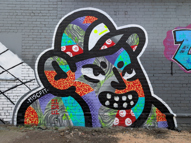 Graffiti of a grinning face wearing a cap, the fill comprises of different patterns in a collage formation