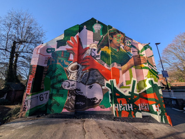 Colourful mural featuring a saxophone player, a woman playing an unspecified woodwind instrument and abstract shapes in bold reds, greens, pinks and blacks, with text including 'The dreamers' and 'Rhythm'