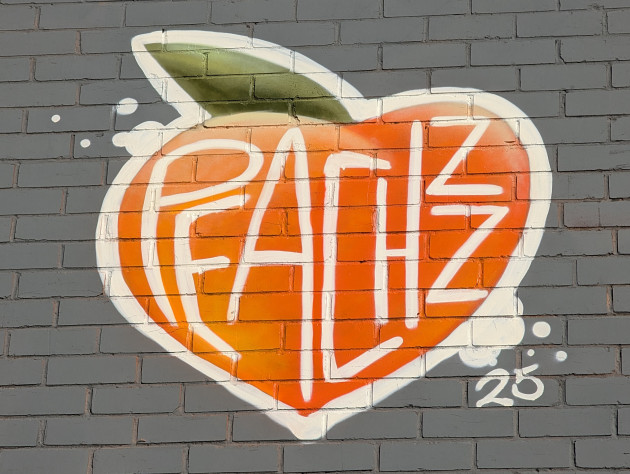 Small mural of a heart shaped orange peach with the artist's name written to fill the shape of the fruit