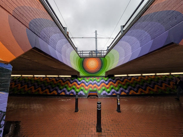 Subway mural featuring a vibrant target-like circle of concentric orange, green and purple rings on a central wall with a zig-zag pattern on the wall below