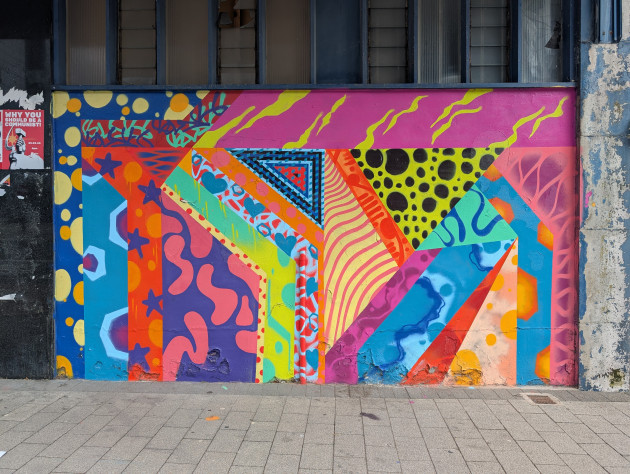 Vibrant, multi-layered abstract mural that uses unusual geometric shapes in a patchwork style to partition the artwork into distinct sections, each shape is filled with a different pattern