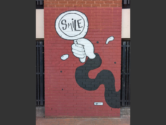 Black and white mural featuring a bendy arm with hand holding a magnifying glass revealing the word 'smile'