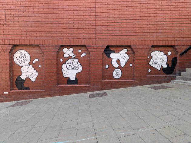 Adam Briscoe mural featuring cartoon style hands holding various items with the word Tarn on