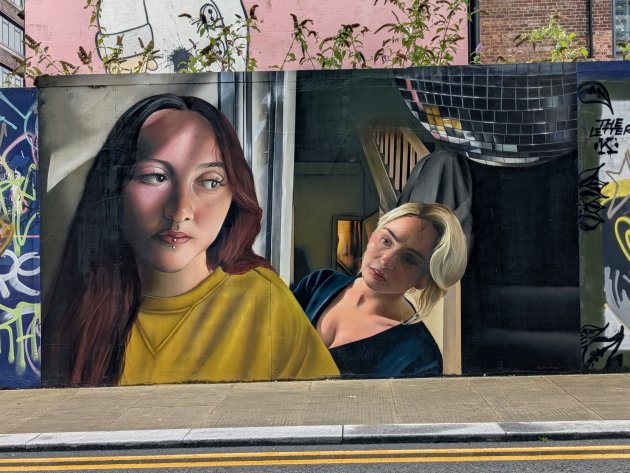 Mural featuring two somber looking women inside a house with a large glitter ball
