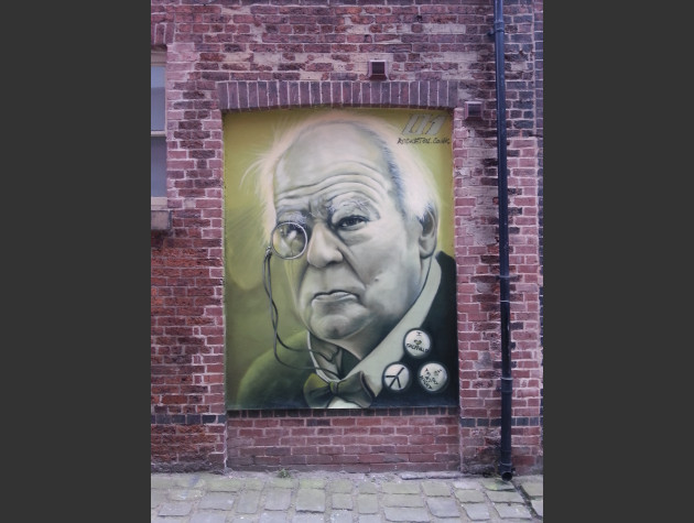 Small wall mural of Sir Patrick Moore painted in a small alcove; on his lapel are three pin badges