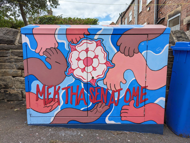 Utility cabinet painted with a white rose and the words 'Mek tha sen at ome' with hands reaching inwards