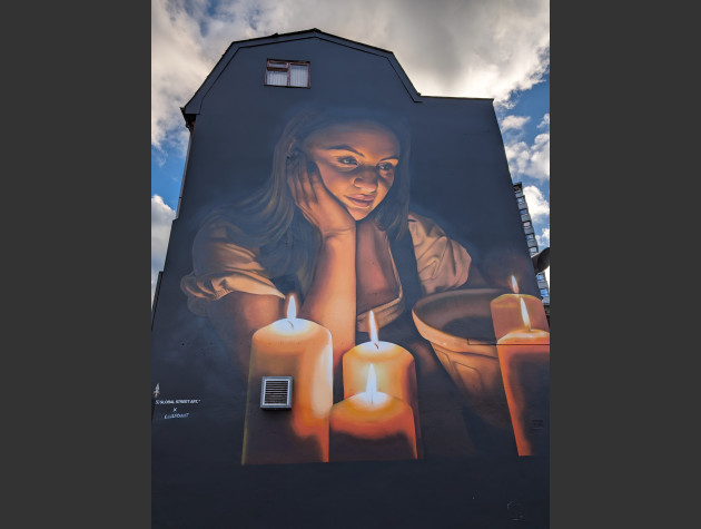 mural of Joan of Arc sat with a pensive look, head resting on her right hand, at a table covered in lit candles and a mixing bowl