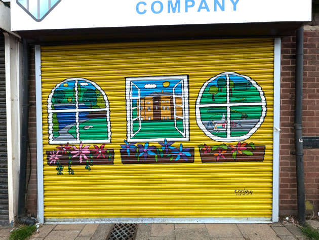 Painted store shutters featuring three windows each with a planter of flowers below