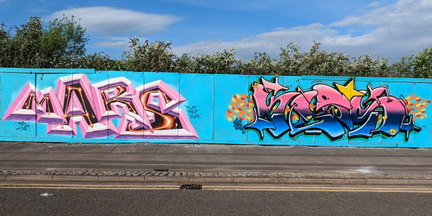 Two wildstyle graffiti pieces side-by-side on some wooden boardings