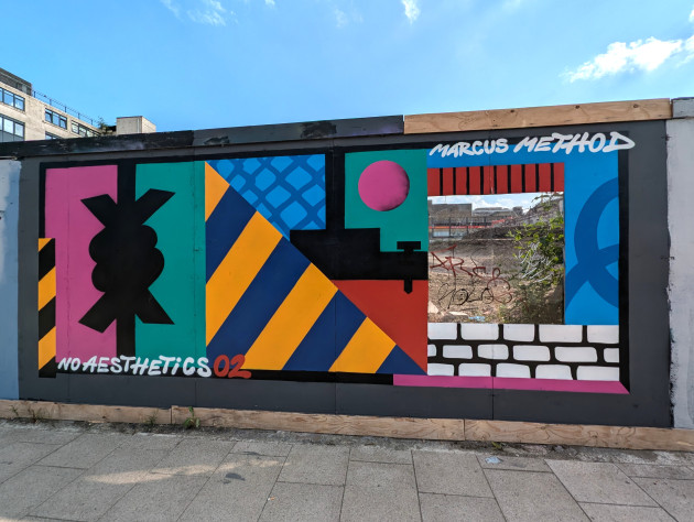 Abstract mural on boardings with a cutout to view the construction site behind