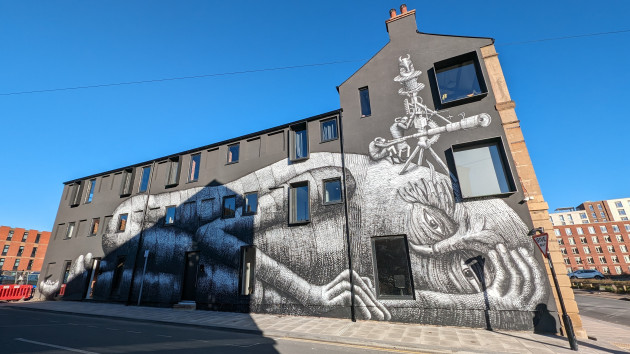 Mural by Phlegm of a giant laying curled up with a couple of astronomers looking out through a telescope set up on the giant's head