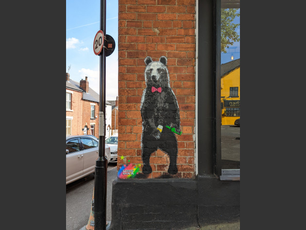 Stencil artwork of a bear pouring beer from a bottle into a glass on the side of The Bear bar