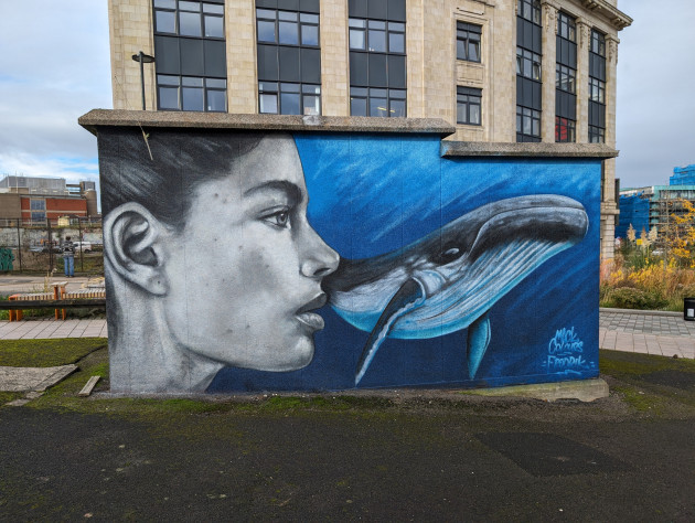 Mural of a woman looking out at an aquatic scene featuring a humpback whale
