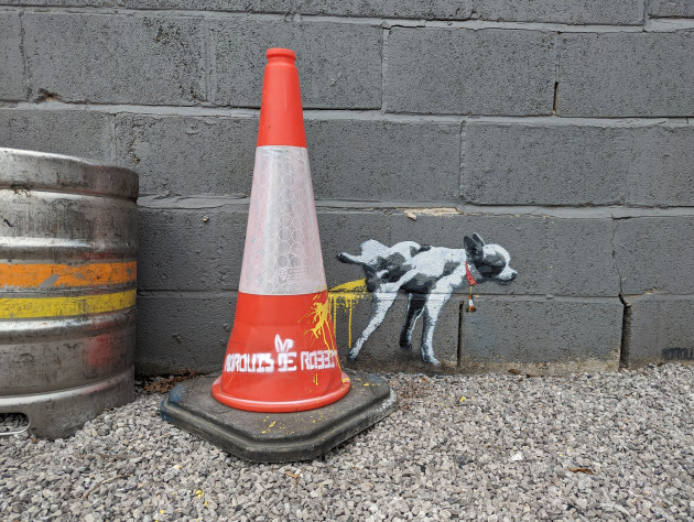 Small mural of a French bulldog pissing against a real traffic cone