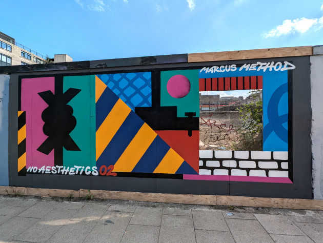 Abstract mural on boardings with a cutout to view the construction site behind
