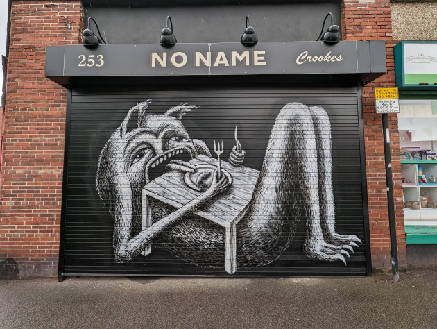 Phlegm artwork on shop shutter depicting a creature layed back with legs extended under a table eating with a knife and fork