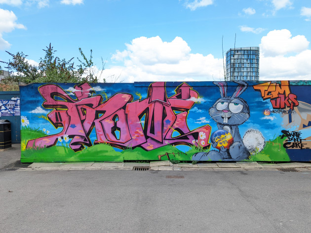 Graffiti writing next to a stoned looking Easter bunny holding a Cadbury's Creme Egg sat in a green meadow with blue skies