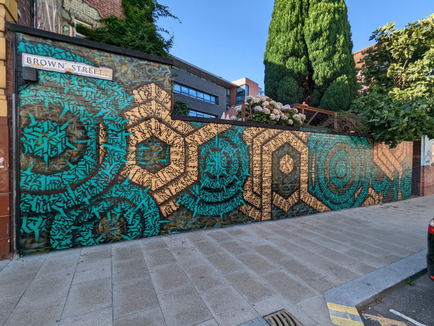 Wall mural made up of golden hexagonal and teal circular shapes using calligraphy as the fill