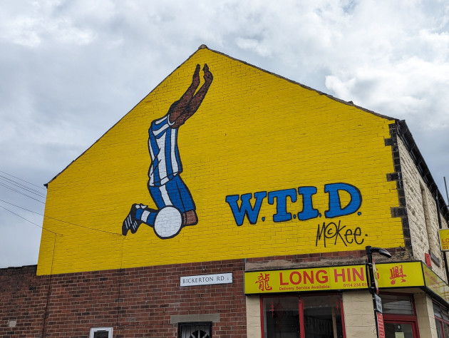 Mural of a black footballer wearing a Sheffield Wednesday kit in a vertical kneel position with arms in the air