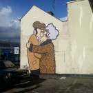 Distant photo of Pete McKee's mural on the side of Fagan's pub with a car park in the foreground