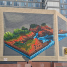 Large mural featuring a hilly landscape made up of layers split across two walls at a slight angle utilising a Trompe L’oeil effect to make it look like a flat surface