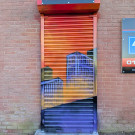 Graffiti mural on a tall narrow metal roller shutter depicting tower blocks against a red sky