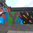 Abstract mural section with bold, clean lines. There's a strong use of bright green, blue and purple. On the right, a pale pink silhouette of a leafy plant stands out against a vivid green background.