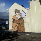 Distant photo of Pete McKee's mural on the side of Fagan's pub with a car park in the foreground