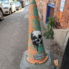 Orange traffic cone sprayed with the tag for the artist Game Over and a picture of a skull