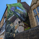Large wall mural on the side of a terraced house featuring a black bird feeding a worm to three young chicks